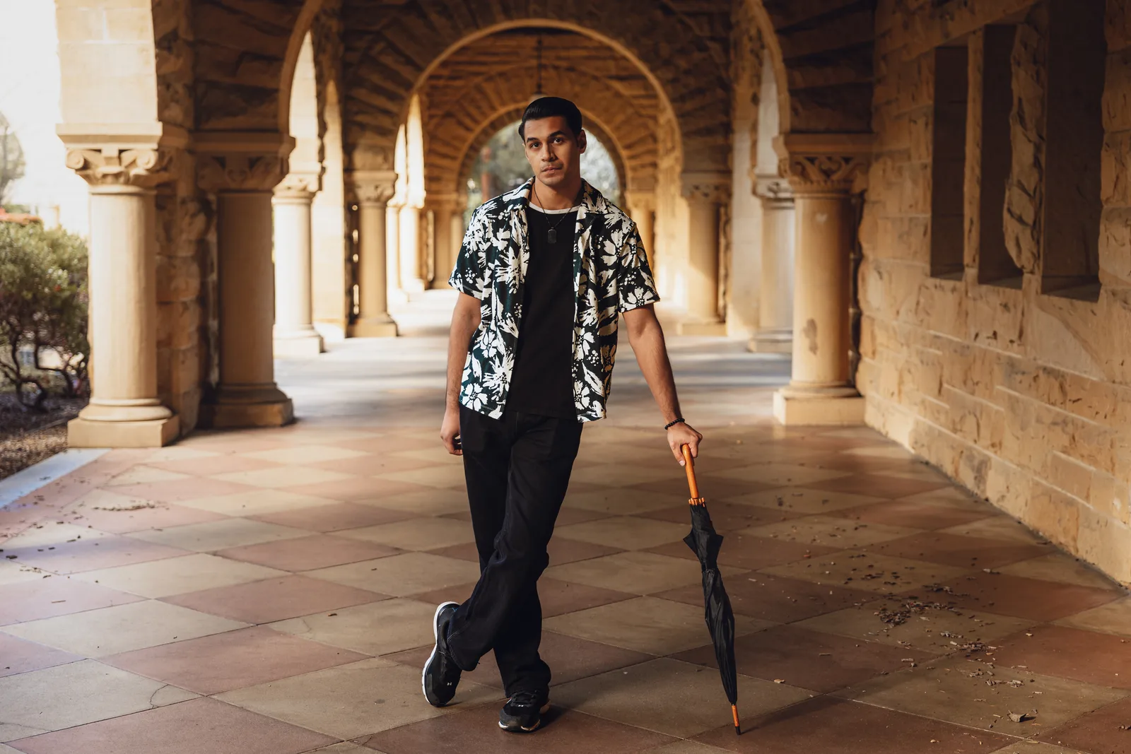 Sagar Shabbir walking through arched corridor with umbrella