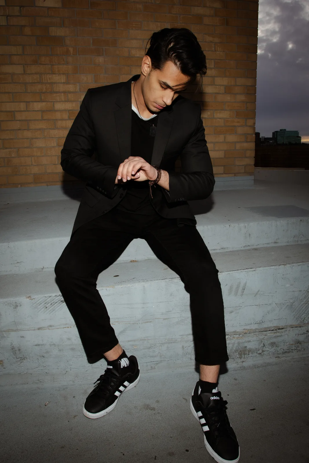 Sagar Shabbir — seated on rooftop steps, black suit, editorial