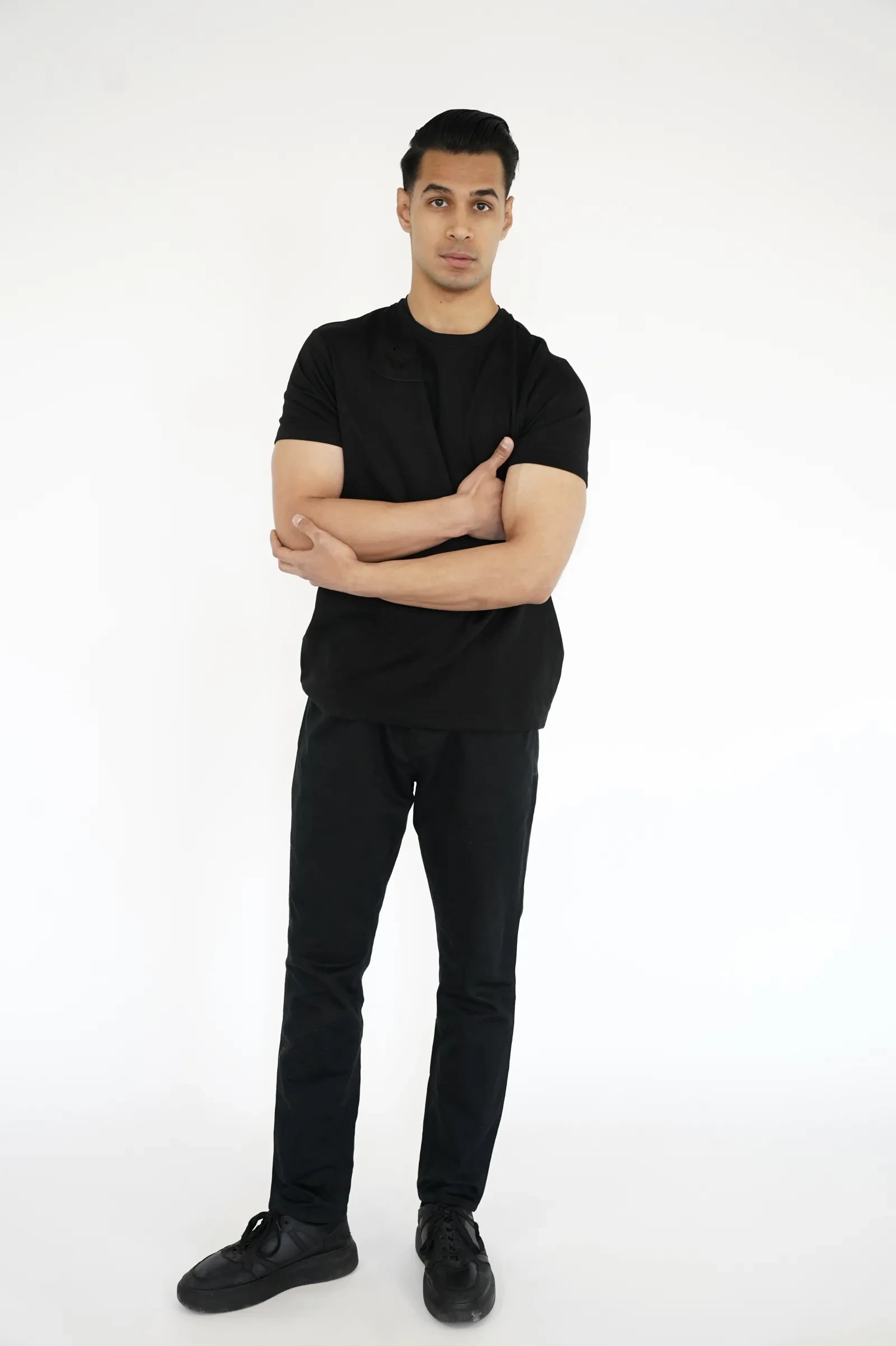 Sagar Shabbir — digital, full-length, black t-shirt and black trousers, arms crossed, studio white background