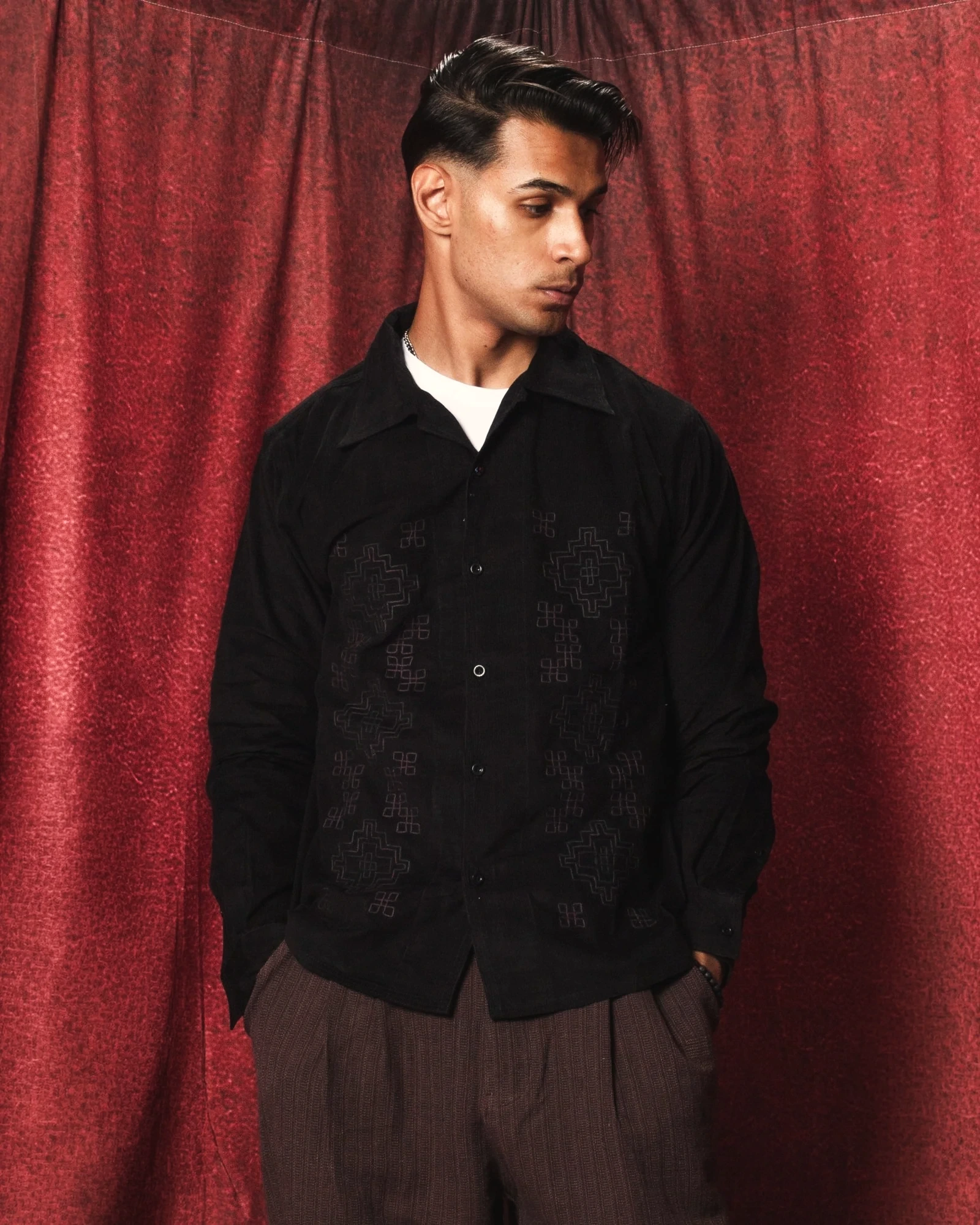 Sagar Shabbir — black embroidered shirt, portrait, red curtain studio