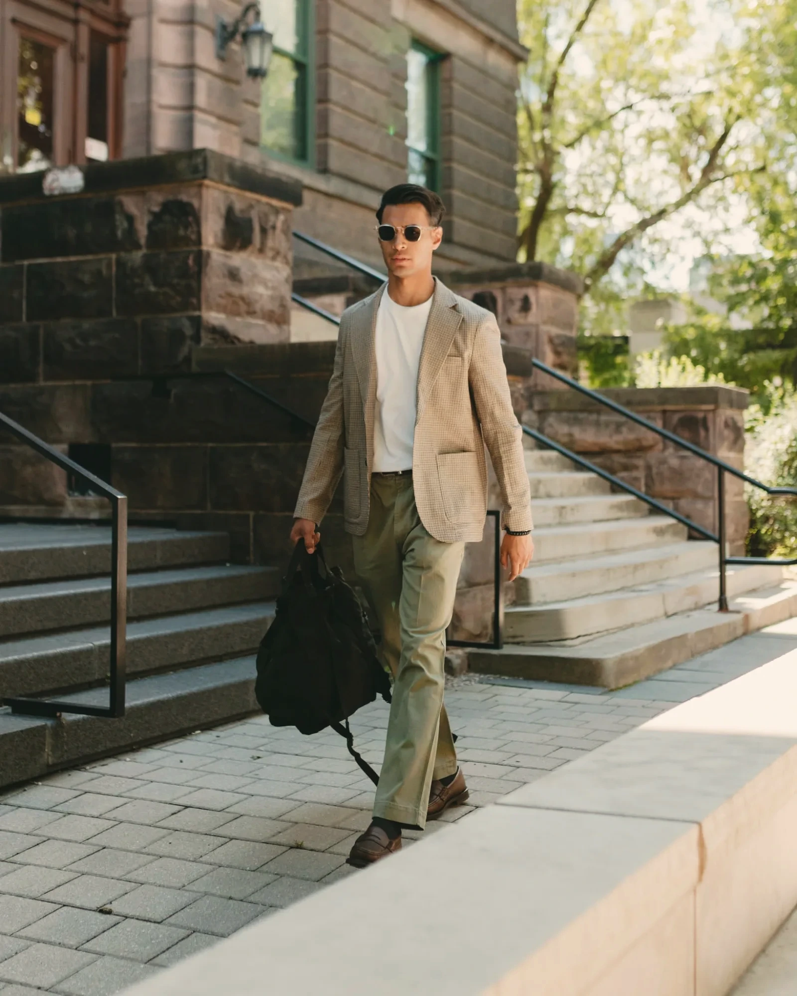 Sagar Shabbir — tan check blazer and olive trousers, walking with bag, lifestyle editorial